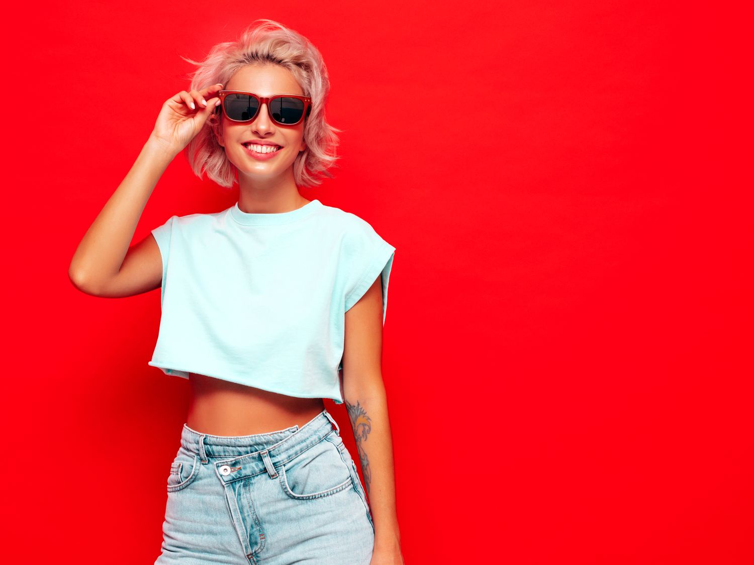 Mulher sorrindo de óculos de sol diante de uma parede vermelha